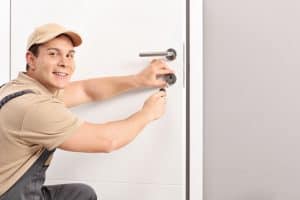 Cheerful locksmith installing a door lock on a new white door and looking at the camera