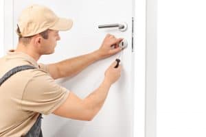 Studio shot of a young male locksmith installing a lock on a white door with a screwdriver isolated on white background